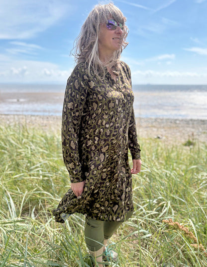 Person wearing a leopard print dress standing on a grassy field with a beach and blue sky in the background