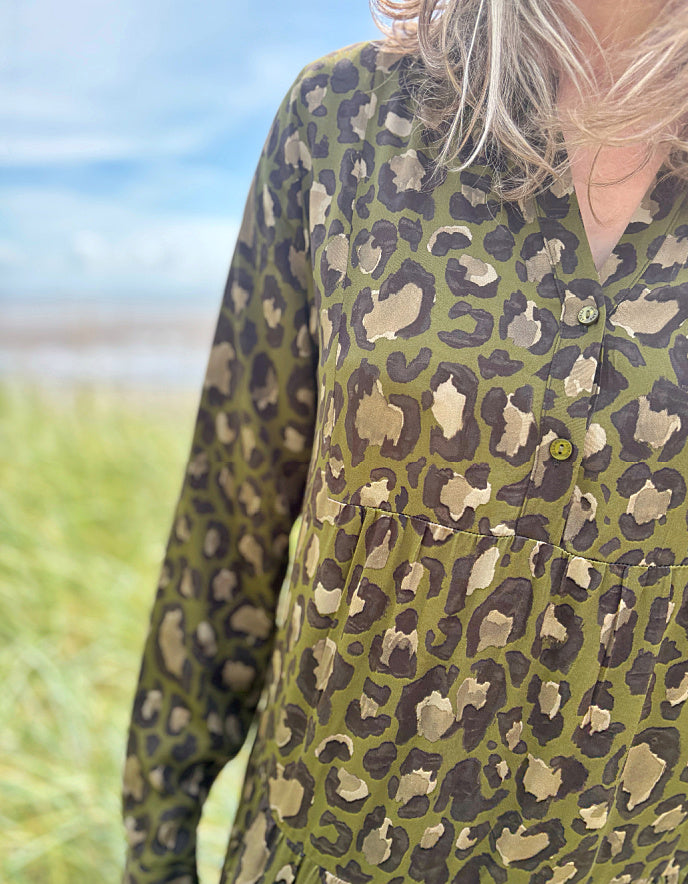 Person wearing a leopard print dress standing on a grassy field with a beach and blue sky in the background