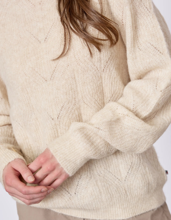 Close-up of a person wearing a cream knitted sweater with a plain background