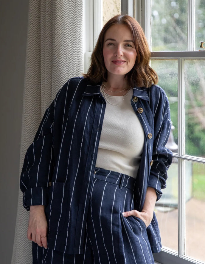 Woman wearing a navy pinstripe outfit standing by a window.