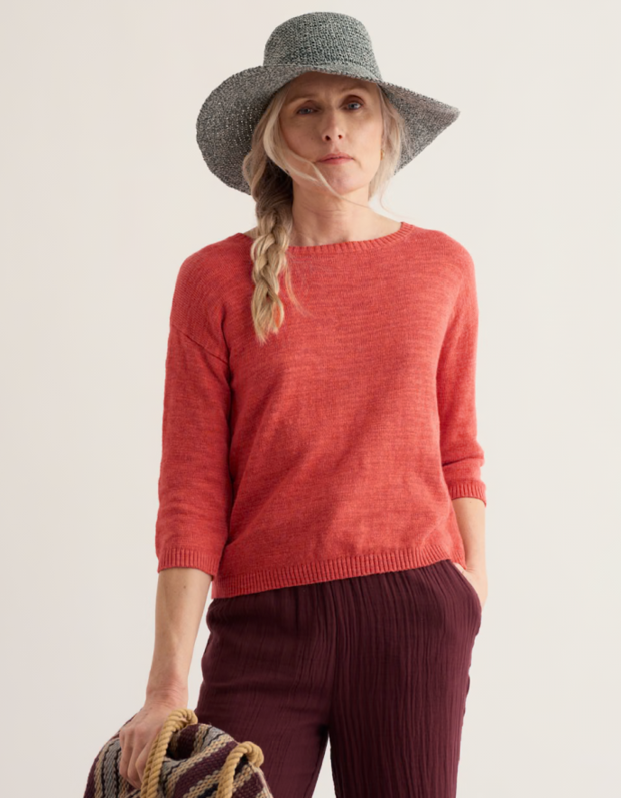 Person wearing a coral red cotton sweater and burgundy pants on a white background