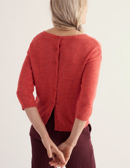 Person wearing a coral red cotton sweater and burgundy pants on a white background