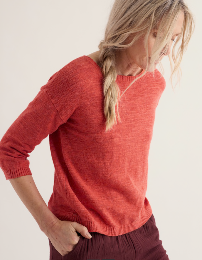 Person wearing a coral red cotton sweater and burgundy pants on a white background