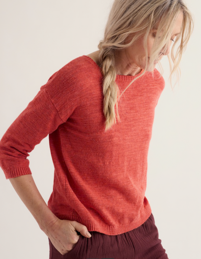Person wearing a coral red cotton sweater and burgundy pants on a white background