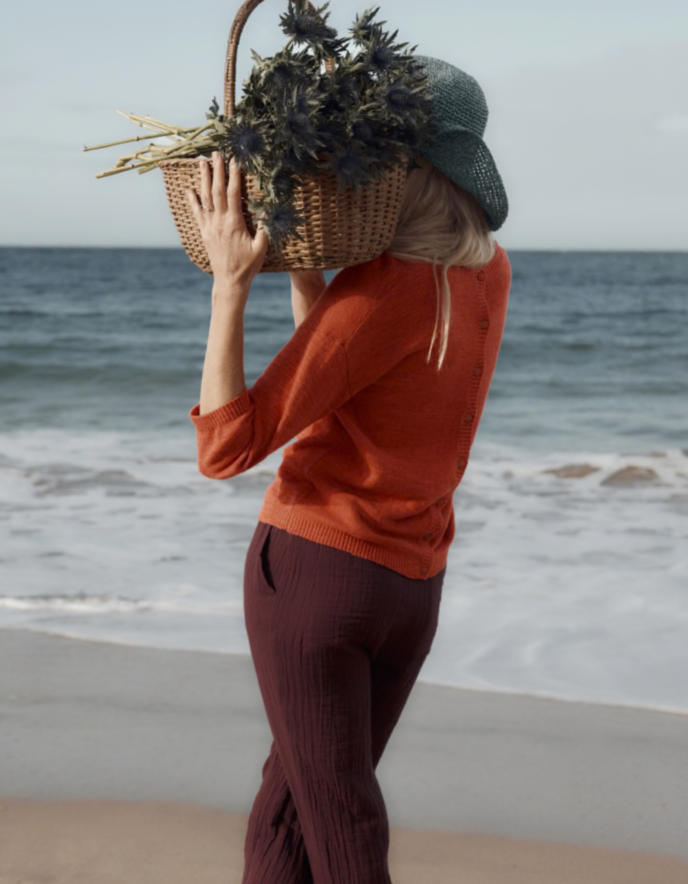 Person holding a woven basket with plants on a beach