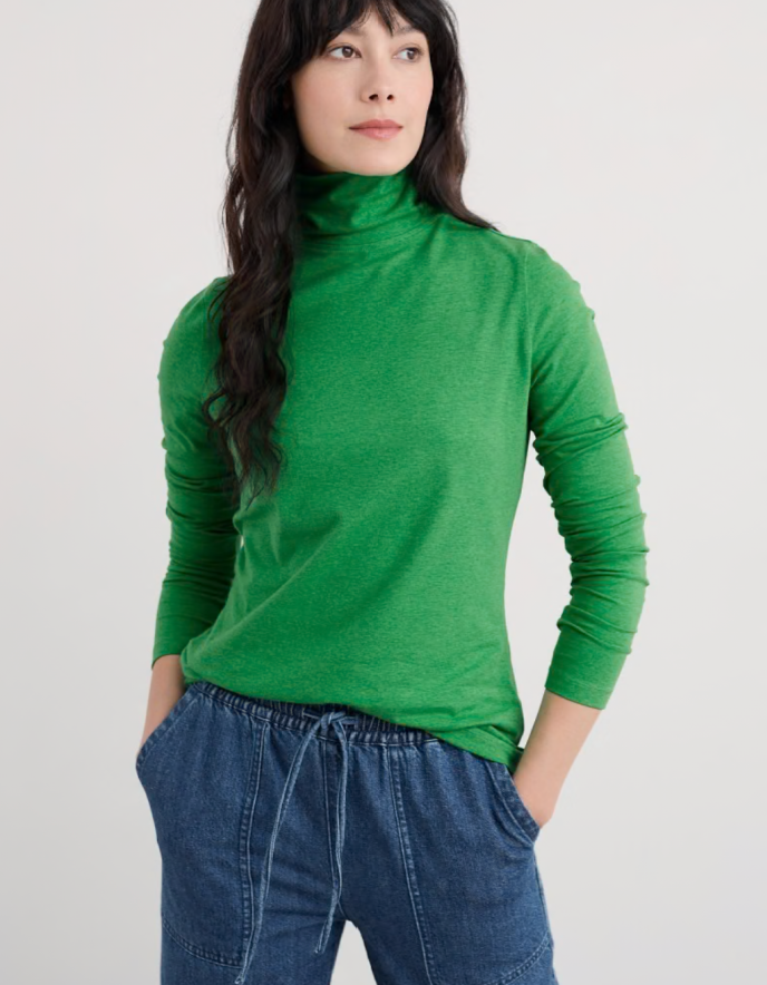 Person wearing a green turtleneck and blue jeans on a white background