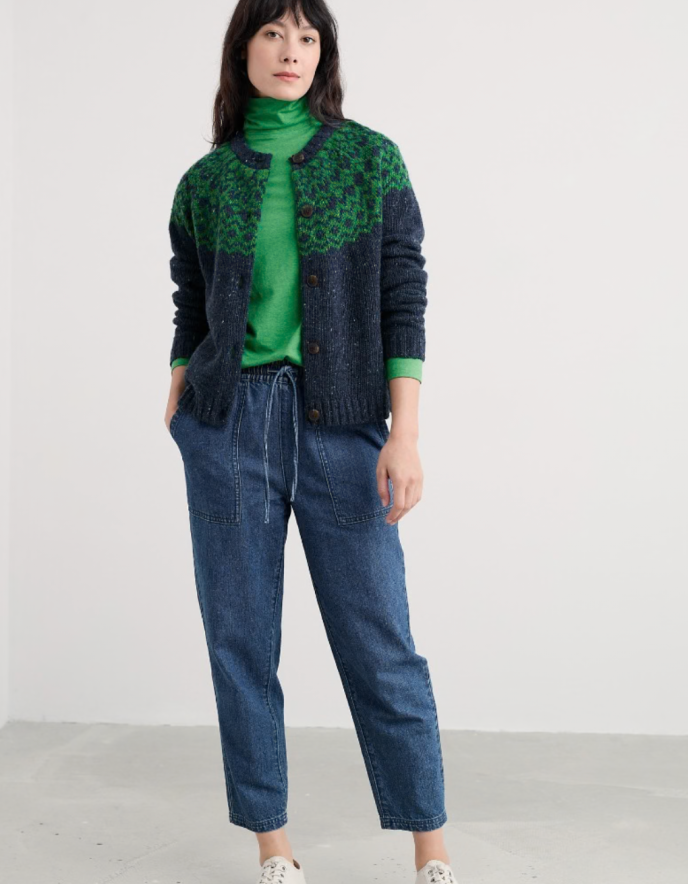 Person wearing a green sweater and blue jeans with a patterned cardigan on a white background