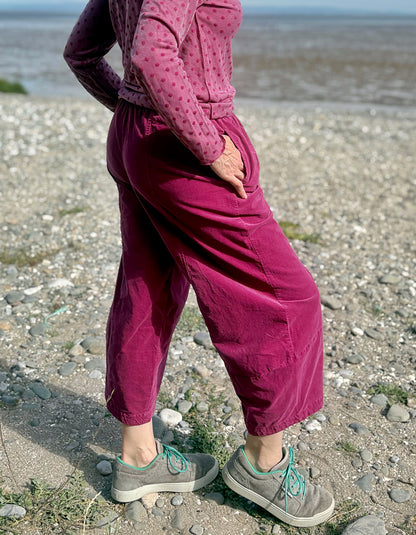 Woman in pink needlecord lantern trousers and a pink pink spotty top standing on a pebbly beach with ocean and sky in the background