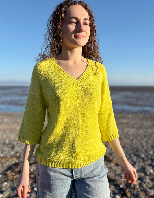 Woman wearing a yellow sweater standing on a beach with ocean in the background