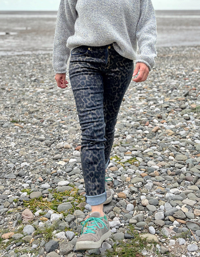 Person wearing a gray sweater and leopard print pants on a rocky surface