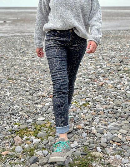 Person wearing a gray sweater and leopard print pants on a rocky surface