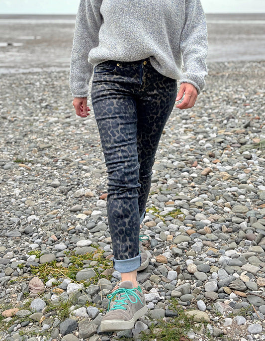 Person wearing a gray sweater and leopard print pants on a rocky surface