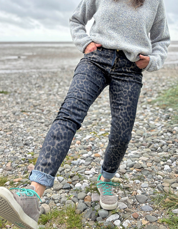 Person wearing leopard print pants and a gray sweater on a rocky beach.