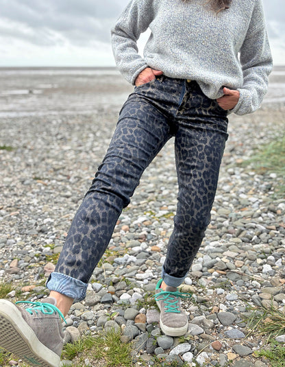 Person wearing leopard print pants and a gray sweater on a rocky beach.