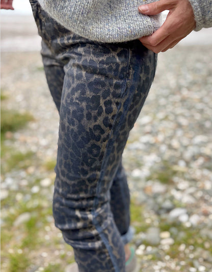 Person wearing leopard print pants and a gray sweater on a blurred natural background