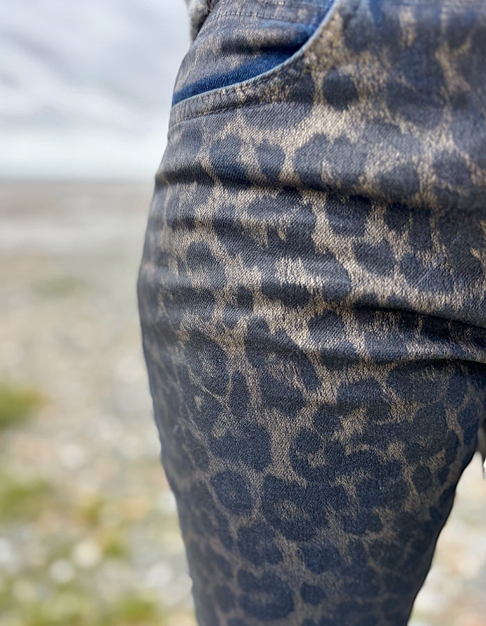 Close-up of a person wearing leopard print pants with a blurred natural background