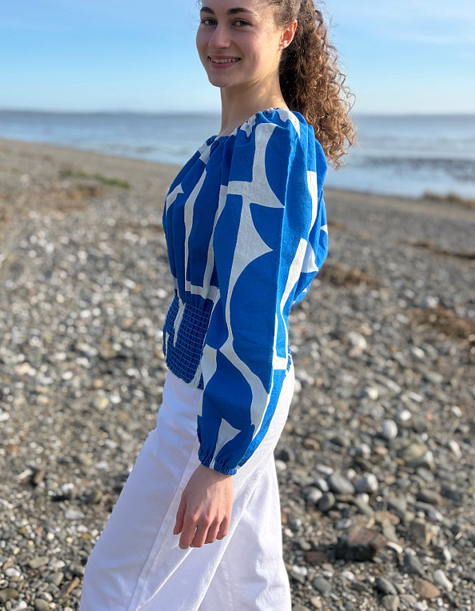 Person wearing a blue and white patterned top on a pebbly beach.