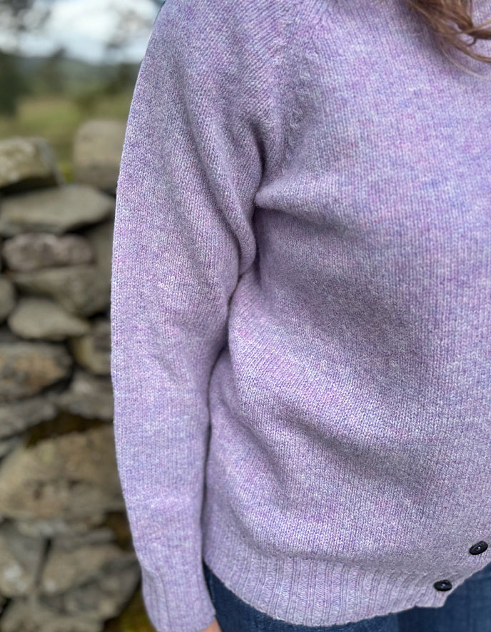 Close-up of a person wearing a light purple sweater with a stone wall background