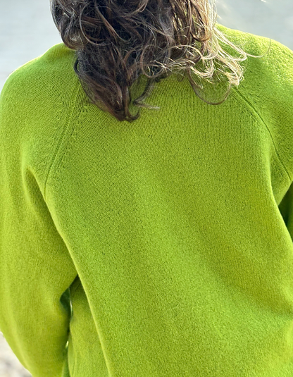 Close-up back view of a person wearing a bright lime green knit sweater, with wavy brown hair visible at the top.