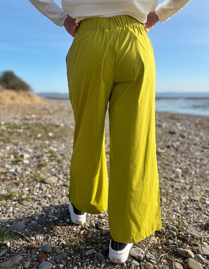 Person wearing bright lime wide leg pants and a white shirt on a pebbly beach.