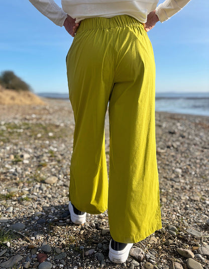 Person wearing bright lime wide leg pants and a white shirt on a pebbly beach.