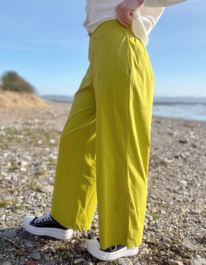 Person wearing bright lime wide leg pants and a white shirt on a pebbly beach.