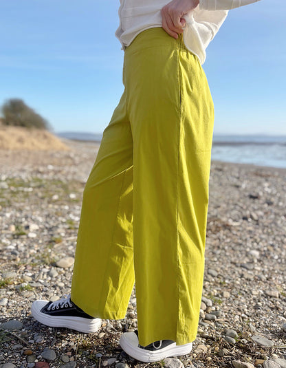 Person wearing bright lime wide leg pants and a white shirt on a pebbly beach.
