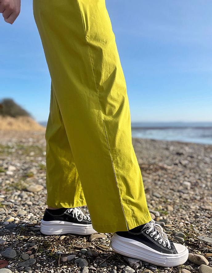Person wearing bright lime wide leg pants and a white shirt on a pebbly beach.