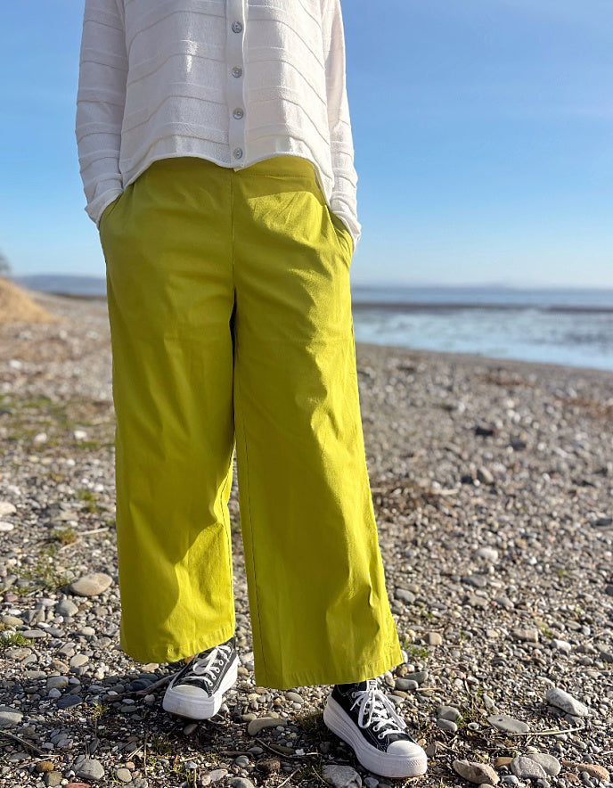 Person wearing bright lime wide leg pants and a white shirt on a pebbly beach.