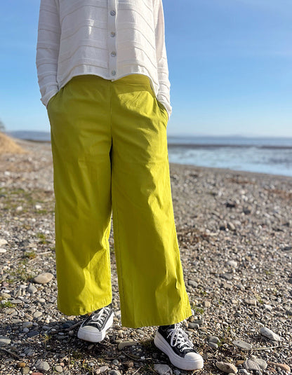 Person wearing bright lime wide leg pants and a white shirt on a pebbly beach.