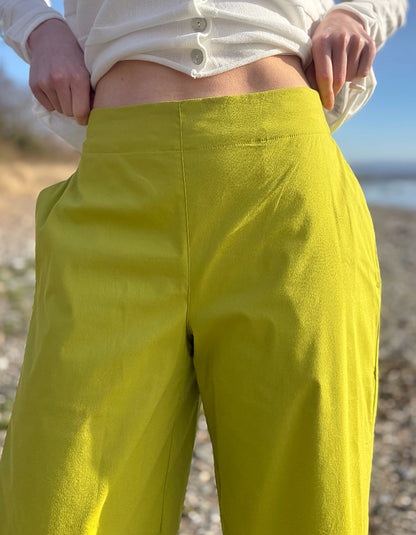 Person wearing bright lime wide leg pants and a white shirt on a pebbly beach.