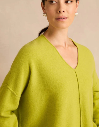 A close-up of a woman wearing a soft, oversized lime green V-neck sweater against a warm beige background.
