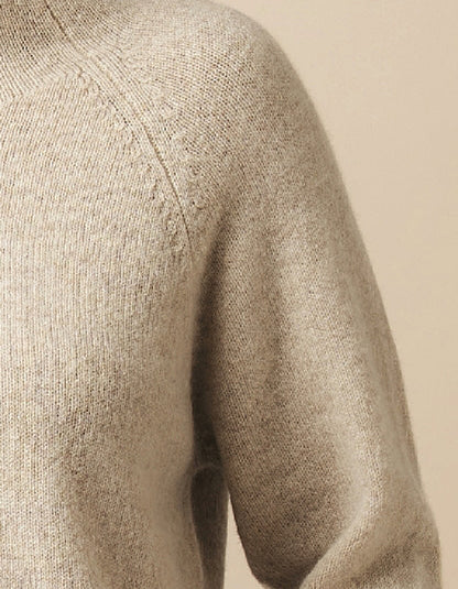 Close-up of a beige knit sweater showing the shoulder, sleeve, and ribbed texture against a matching neutral background.