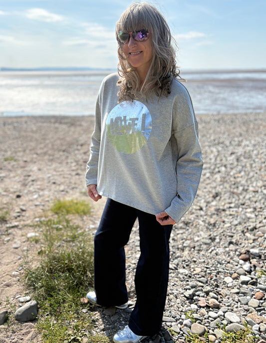 Person wearing a grey cotton  sweatshirt with a silver graphic design that says LOVE