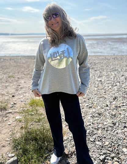 Person wearing a sweatshirt with a 'lovel' graphic design on a beach.