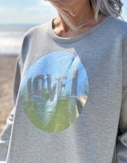 Gray sweatshirt with a circular design featuring 'LOVE' and nature imagery, worn by a person outdoors.