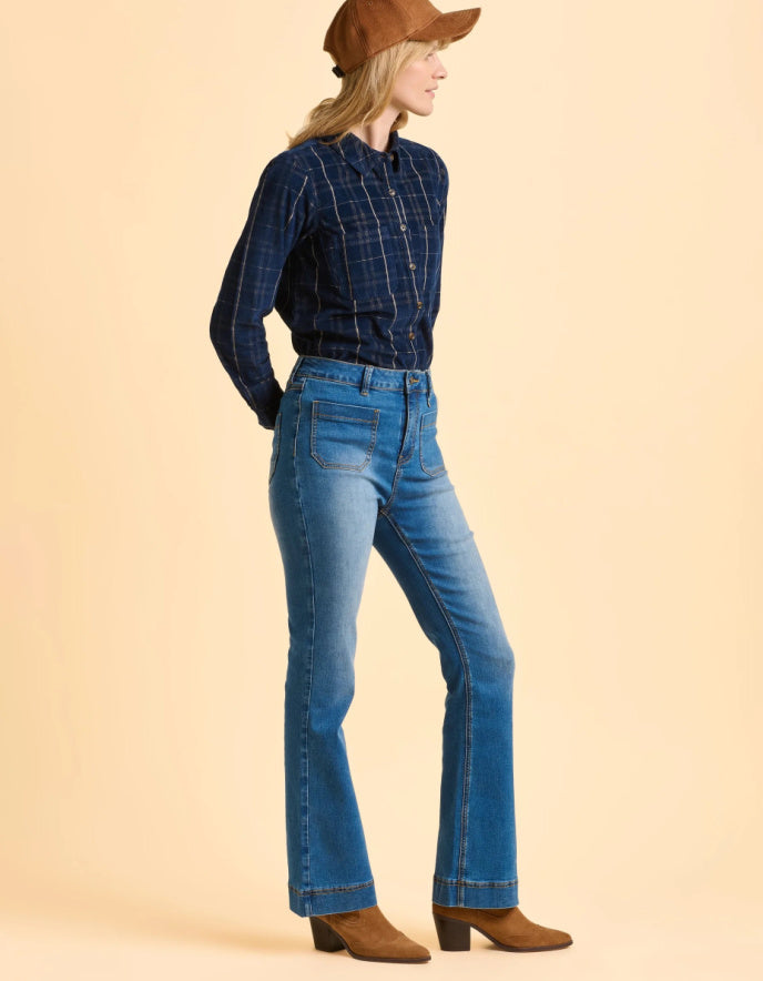 Woman wearing a blue plaid shirt and jeans with a brown hat on a beige background