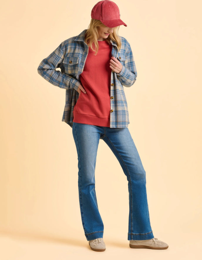 Person wearing a plaid shirt, red cap, pink shirt, blue jeans, and gray shoes on a beige background