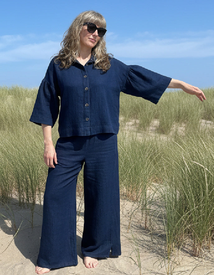 Woman in a navy outfit standing on a beach with grass and sand.