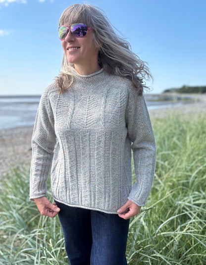 Person wearing a donegal tweed wool grey sweater with wide leg jeans and sunglasses on a beach