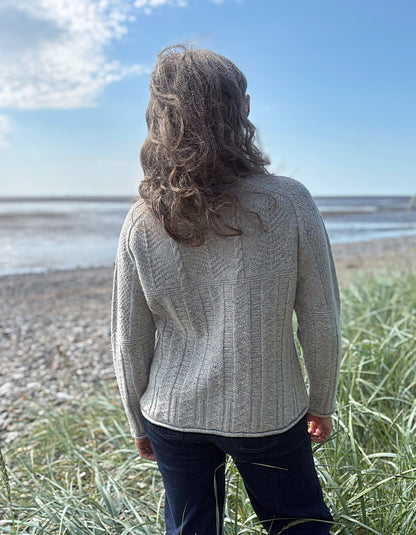 Person wearing a donegal tweed wool grey sweater with wide leg jeans and sunglasses on a beach
