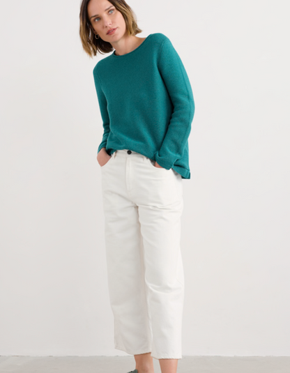 Woman wearing a teal sweater and white pants on a white background