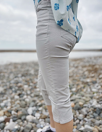 Person wearing light gray capri pants on a pebbly beach.