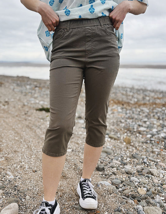 Person wearing brown capri pants standing on a pebbly beach.