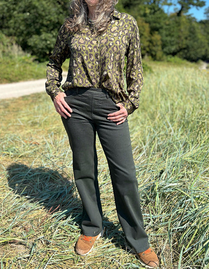Person wearing a camouflage shirt and dark green jeans standing in a grassy field.