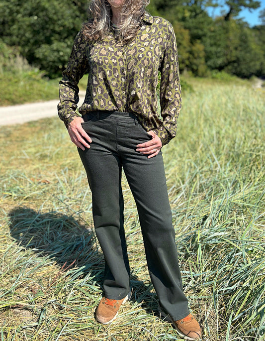 Person wearing a camouflage shirt and dark green jeans standing in a grassy field.