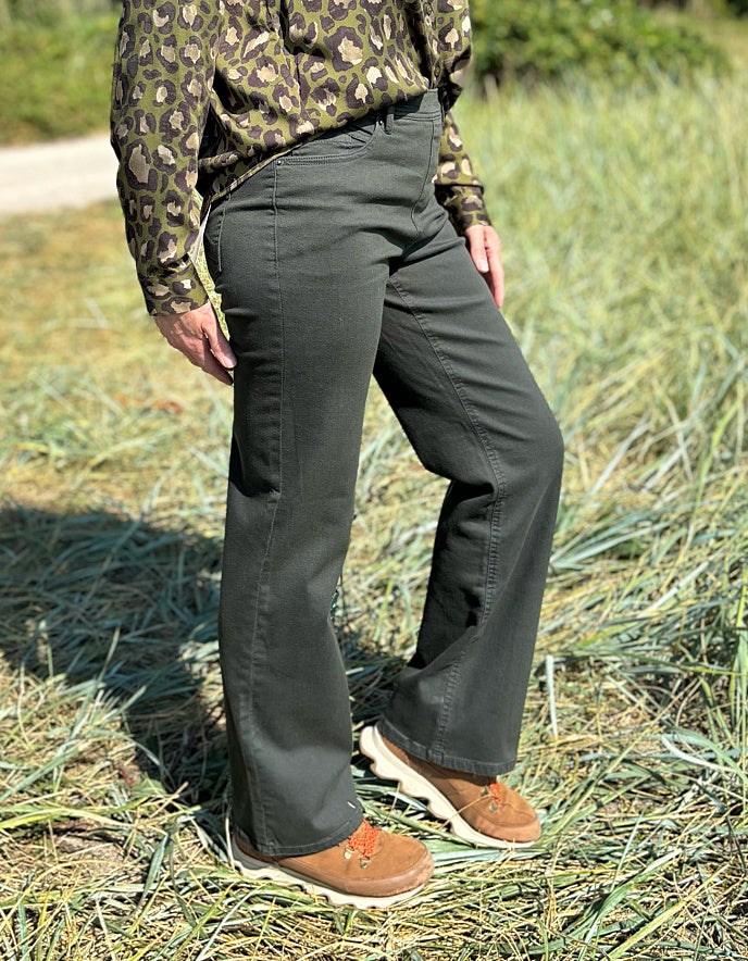 Person wearing camouflage shirt and dark green jeans standing in grassy field