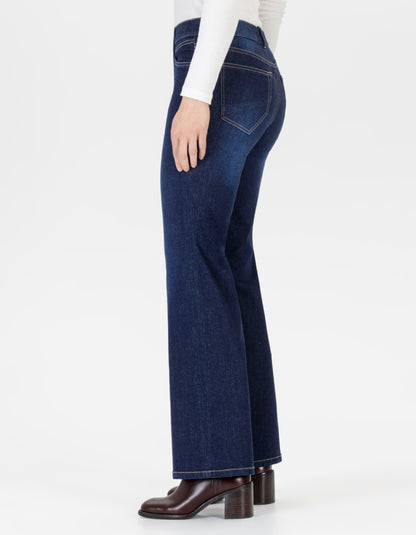 A side profile view of a model wearing dark blue flare jeans, a white long-sleeve top, and brown block-heel boots against a plain white studio background.