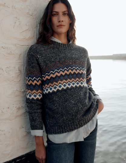 Woman wearing a dark grey tweed sweater with fair isle patterned against a white background