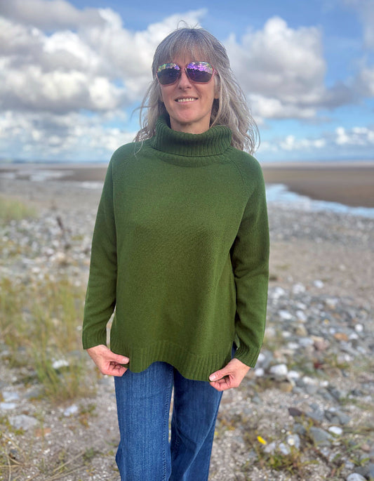 Person wearing a green sweater and sunglasses standing in a rocky landscape with a blue sky.